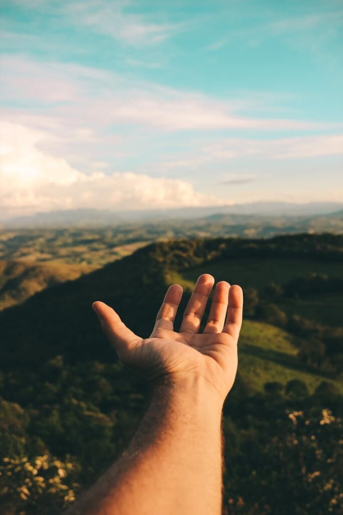 A hand reaching out towards a scenic view of mountains and sky, depicting freedom and exploration.